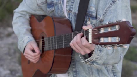 toma cortada del mástil de la guitarra mientras un hombre la toca con una chaqueta vaquera, detalle de las cuerdas y los trastes mientras rasga con la mano