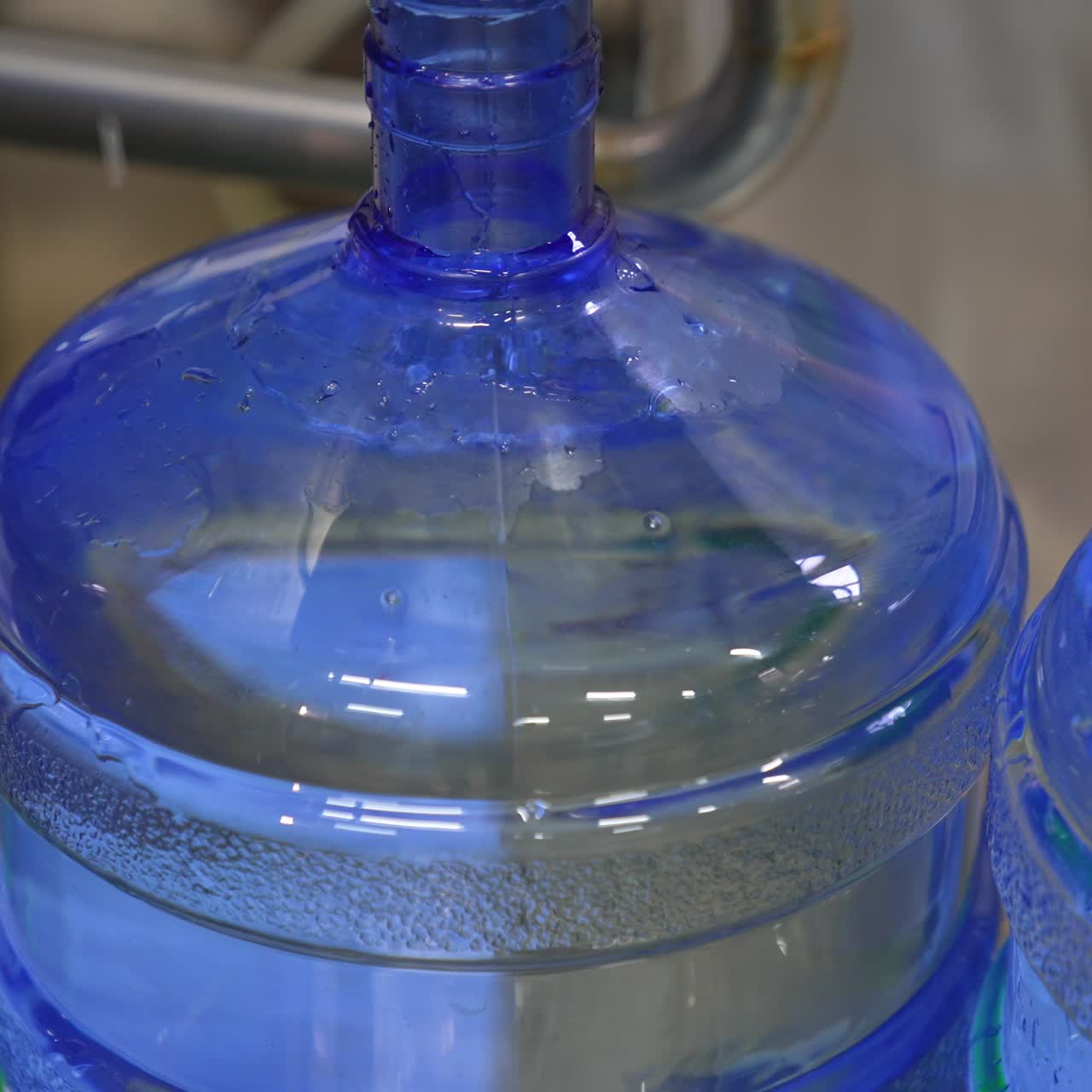 Big bottle is quickly filled with fresh water. Full bottle is moved by the conveyor line. Close up. Food factory concept
