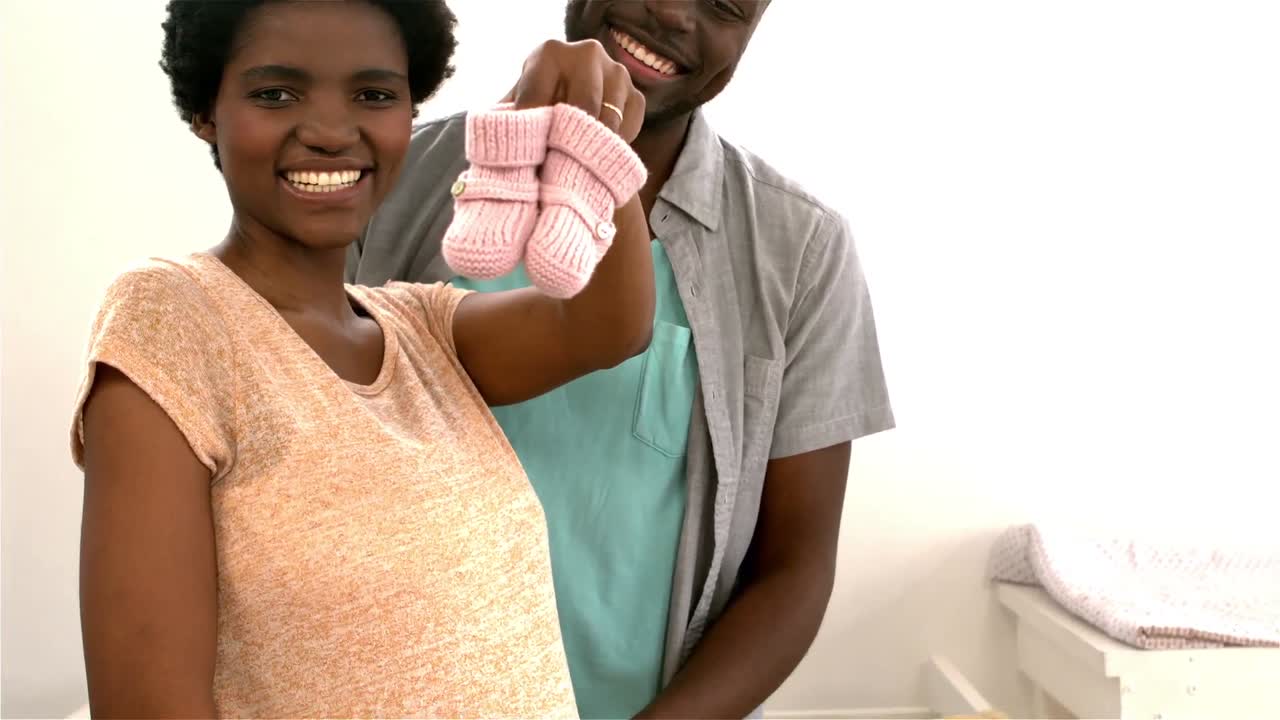 Happy couple holding pink wool baby shoes
