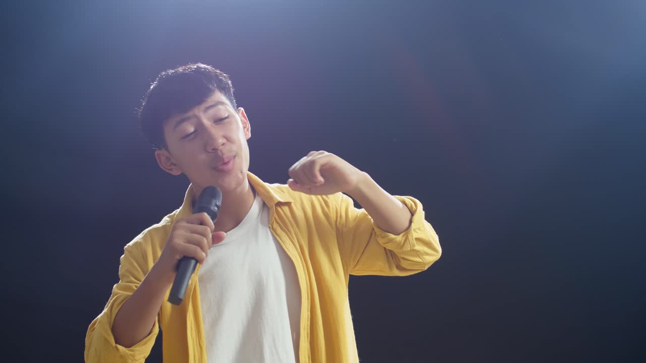 젊은 아시아 소년 이 마이크 를 들고 검은 바탕 에  을 하고 있다
