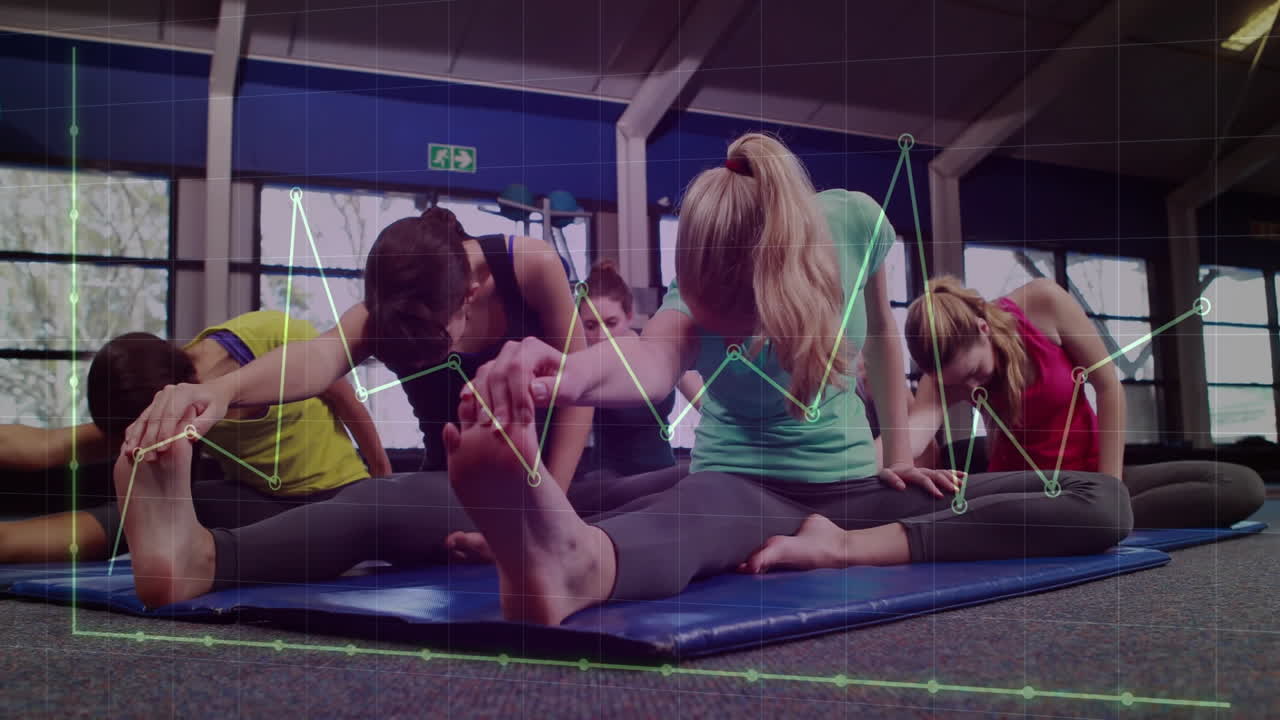 Women in fitness class performing seated leg stretches on blue mats, showing digital graph overlay
