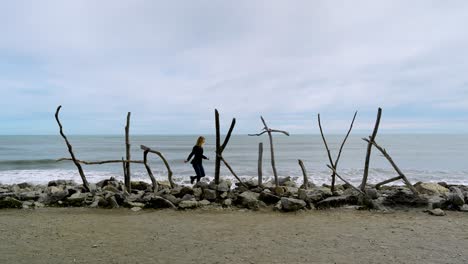 Hokitika Beach sign crafted from driftwood, standing against a coastal landscape on New Zealand’s West Coast as adventurous traveler hops and skips along rocks