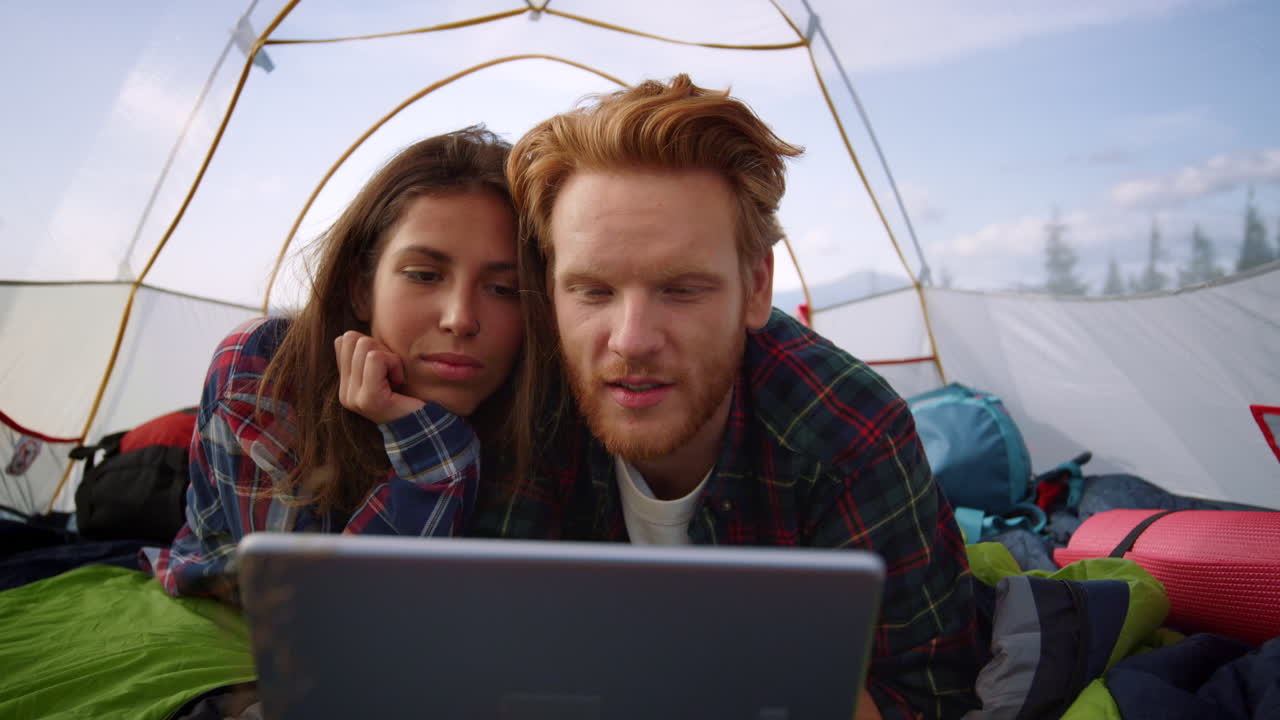 Focused woman and man watching movie on tablet computer in tent