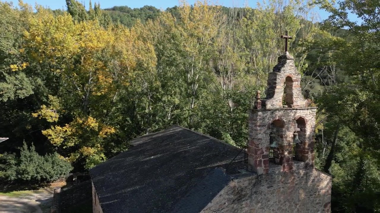 Vista aerea con drone del campanile a vela di San Miguel de Xagoaza che si erge sopra il tetto in pietra della chiesa, incorniciato da alberi fitti nei tranquilli dintorni rurali di Valdeorras, Galizia, Spagna