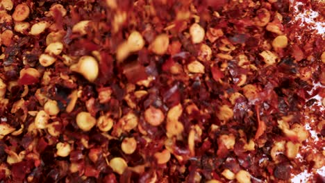dried chili flakes cascade onto a white surface, creating a vibrant, textured pattern in bright lighting