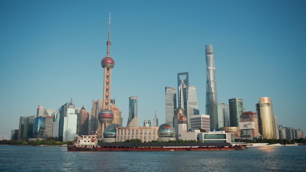 Horizonte de Shanghái con rascacielos ribereños, la Torre Perla Oriental iluminada por el sol y modernas torres de cristal elevándose sobre el río Huangpu, buque de carga cruzando el primer plano, reflejos brillantes, azul claro.
