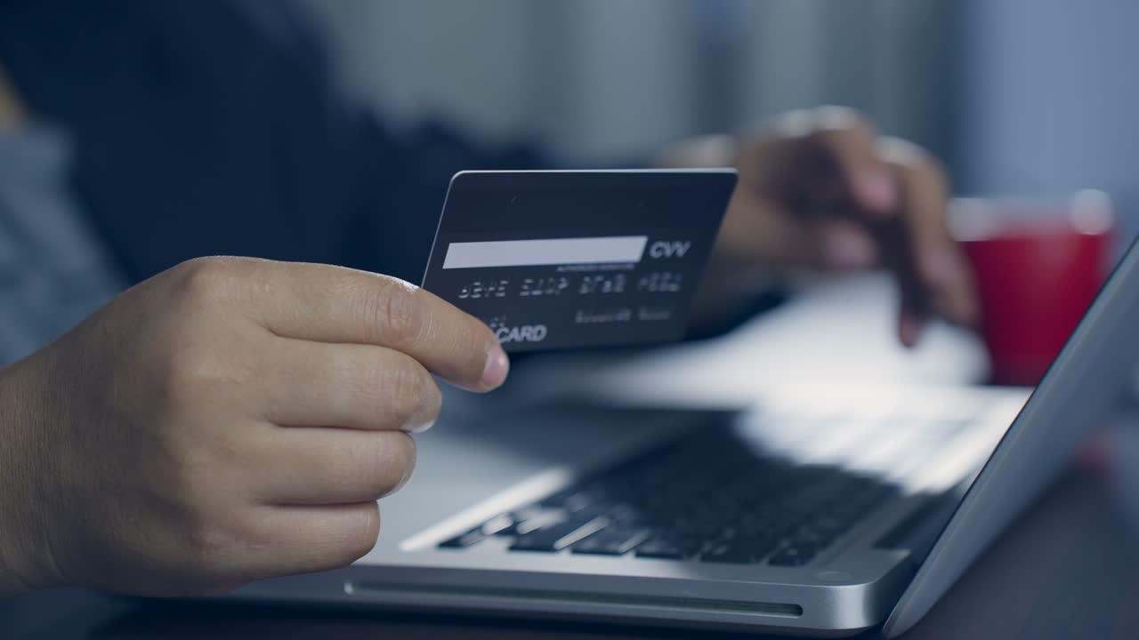 b rodar el movimiento lento de la mano escribiendo el teclado y haciendo compras en línea mientras sostiene la tarjeta de crédito. el titular de la tarjeta sostiene la carta de crédito haciendo pago en línea de e-bank. pagar por la compra en la tienda web usando una computadora portátil