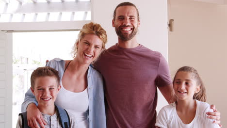 retrato de una familia sonriente de pie junto a la puerta principal abierta en la sala de estar de la nueva casa