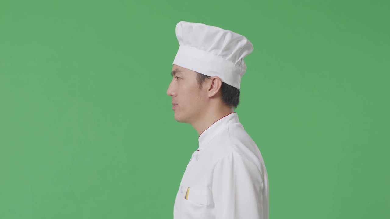 Vista laterale di uno chef asiatico che cammina nello studio con sfondo green screen