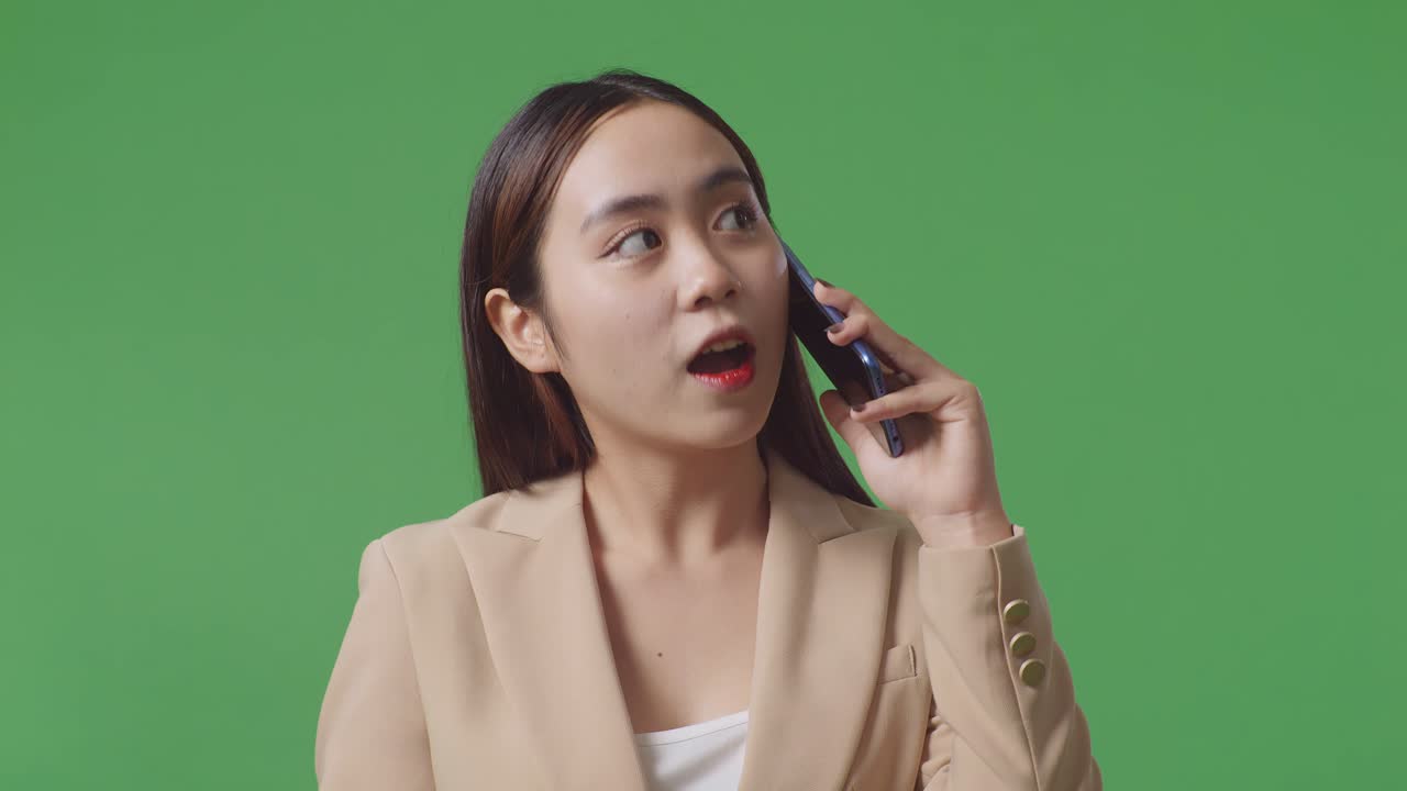미소 짓는 아시아 사업가 여성이 스튜디오에서 녹색 화면에서 휴대 전화로 이야기하고 있습니다.