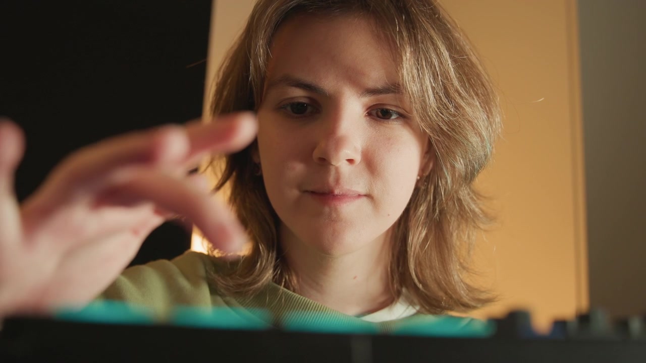 Creator in warm home studio reaches toward audio controller, fingers hovering over pads and knobs while making precise adjustments; focused posture, soft blur, and intimate close view