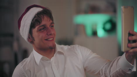 happy man in santa hat taking selfie through digital tablet at dark home