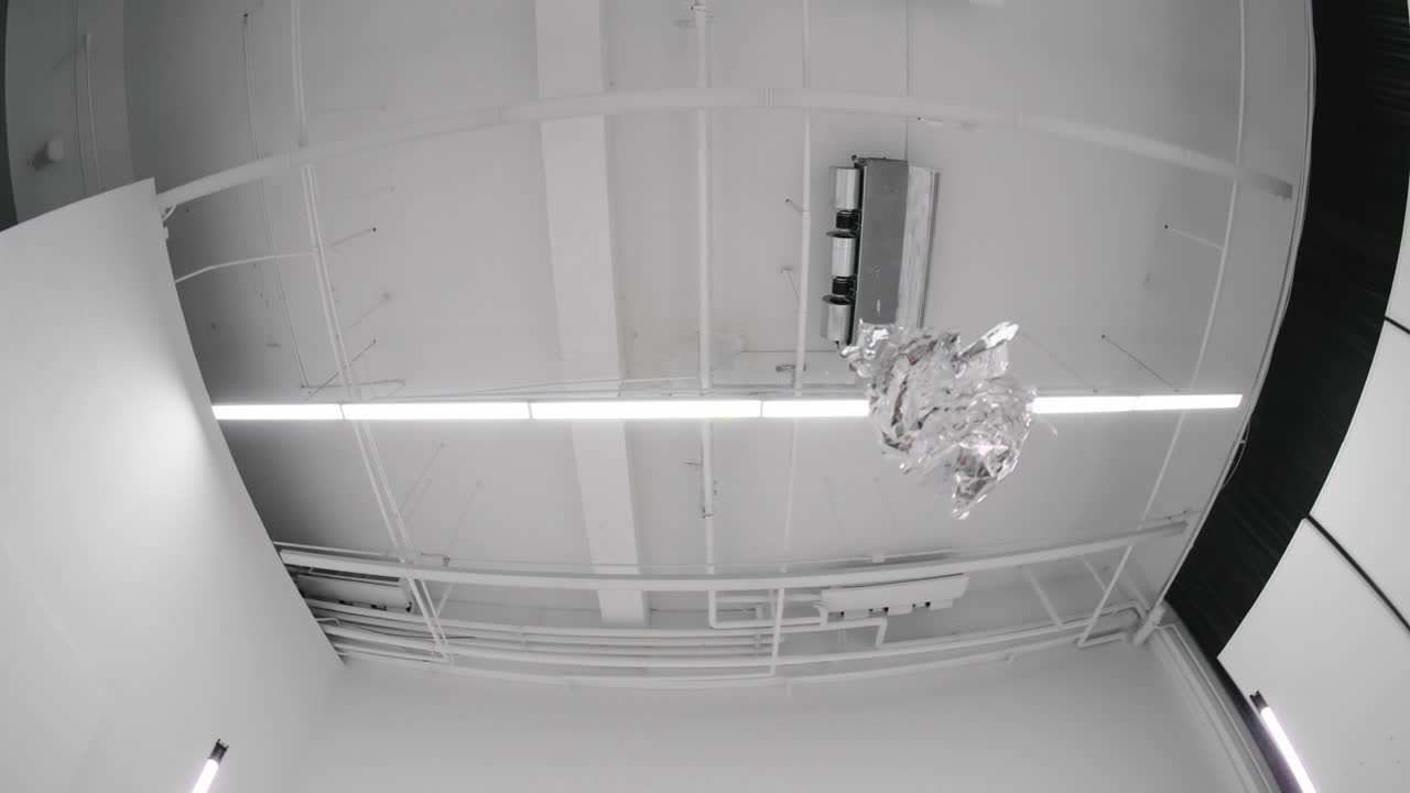 Slow-motion abstract video of tinfoil flying through the air in a studio. Dynamic motion captured with fisheye lens. Shiny metal texture, creative visuals, artistic experimental shot.