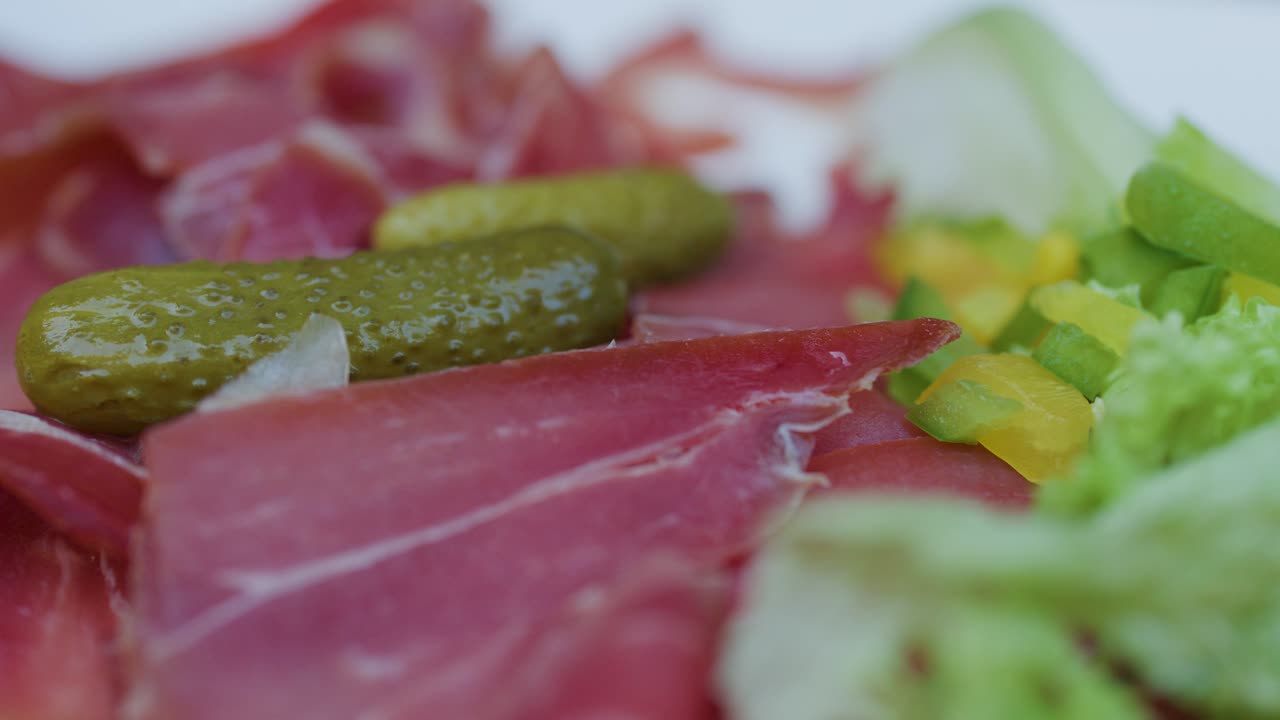 Close-up of hand grabbing ham slice from charcuterie plate with pickle, lettuce, and peppers