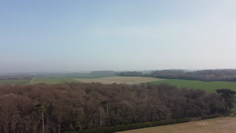 flying over woodland in english countryside with brown and green fields in the background
