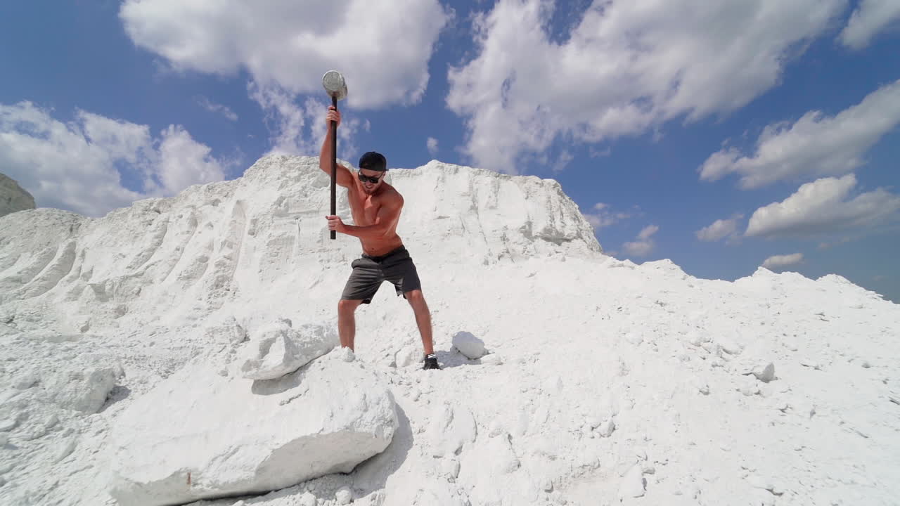 Sportsman with hammer on the hill. Shirtless athlete training with hammer on white mountain in summer. Handsome man with muscular body outdoors.