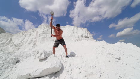 sportsman with hammer on the hill. shirtless athlete training with hammer on white mountain in summer. handsome man with muscular body outdoors.