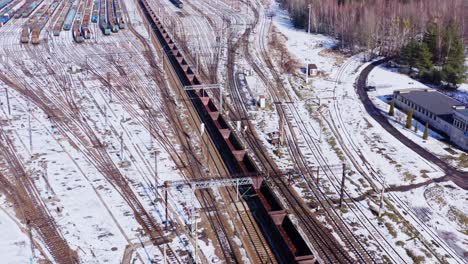 Toma-Aérea-De-Un-Dron-Siguiendo-Un-Largo-Tren-De-Carga-Vacío-A-Través-De-Los-Paisajes-Invernales-Cubiertos-De-Nieve-De-Katowice,-Polonia