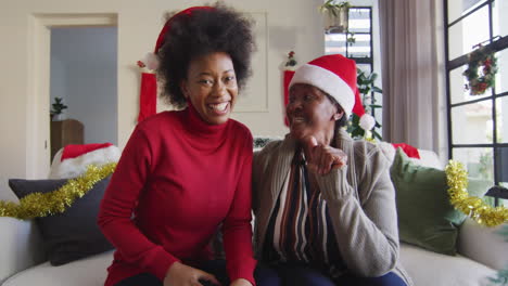 happy african american mother and adult daughter in santa hats on christmas video call, slow motion