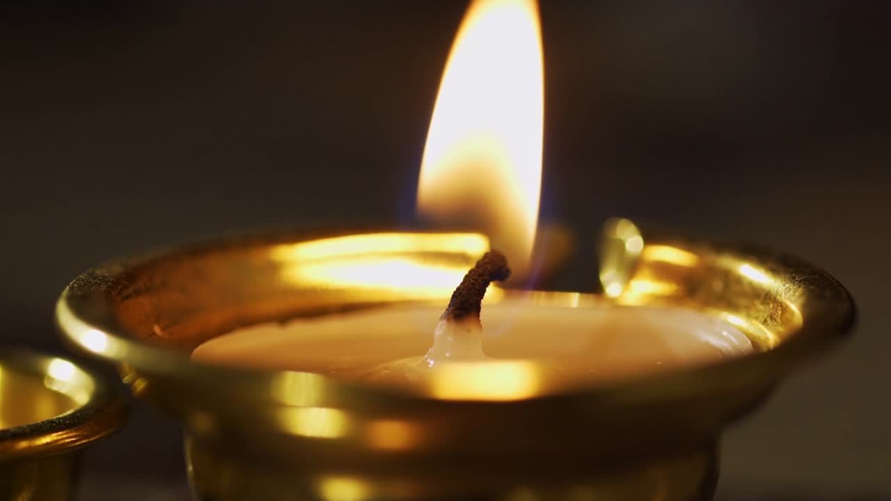Flickering flame burning cotton wick on brass oil lamp in dim room, with melted oil ripples