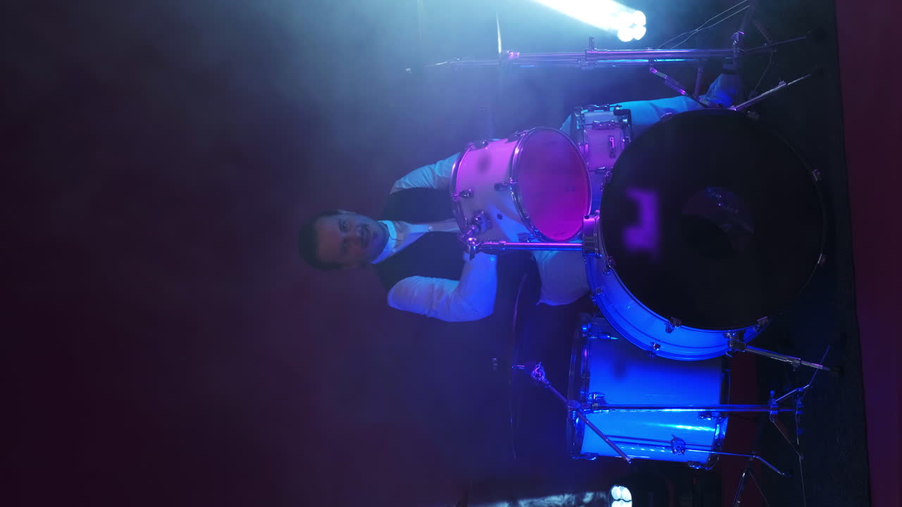 Cool grunge rock musician playing drums on stage doing an amazing metal solo lit by club neon red and blue lights.