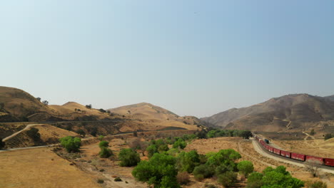 A-freight-train-remains-motionless-amid-a-landscape-burned-black-by-southern-California-wildfires---aerial-pull-back-view