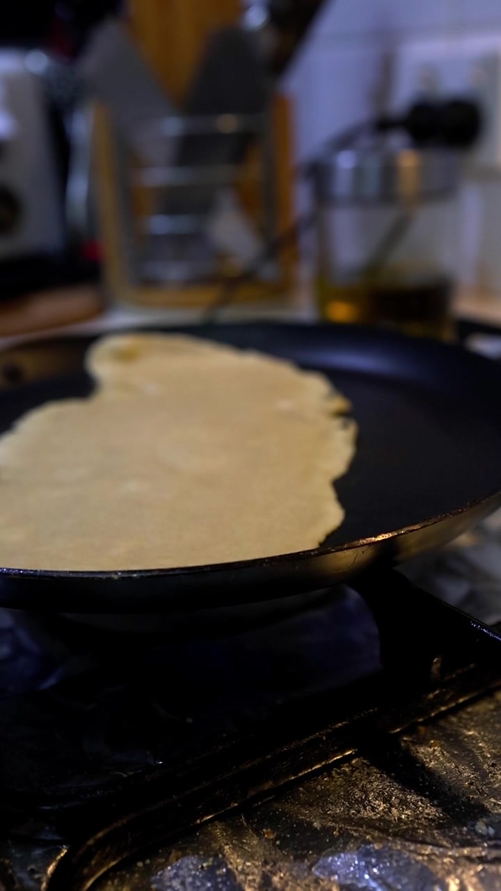 Pastella per crêpes che frigge su una padella nera su un fornello a gas in una cucina