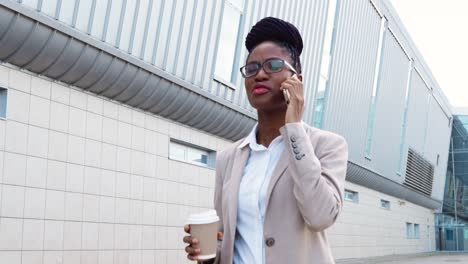 African-american-businesswoman-in-stylish-clothes-and-glasses-talking-on-the-smartphone-and-holding-coffee-to-go-in-the-street