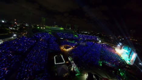 Aerial-flyover-big-stage-with-crowd-of-people-and-flashing-lights-during-festival-on-stage-at-night---Establishing-drone-shot