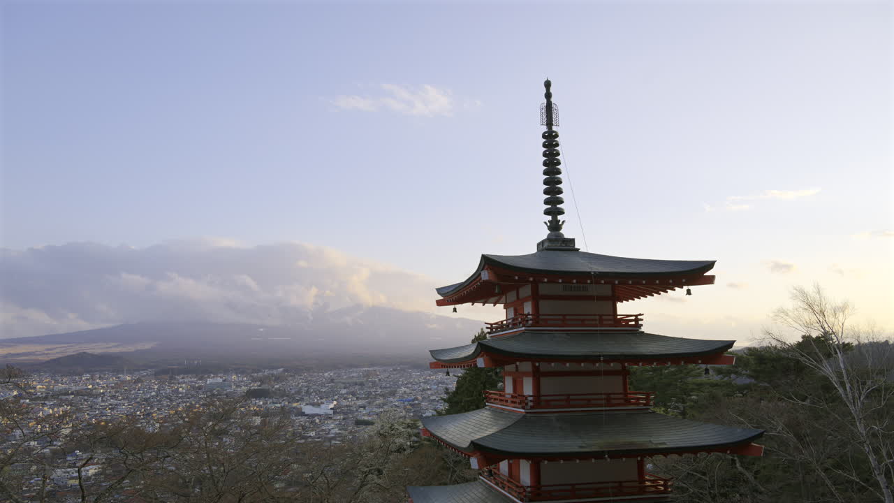 Chureito Pagoda stands tall, overlooking a sprawling Fujikawaguchiko city as the sun sets behind majestic Fuji mountain. The colorful architecture contrasts beautifully with the evening sky