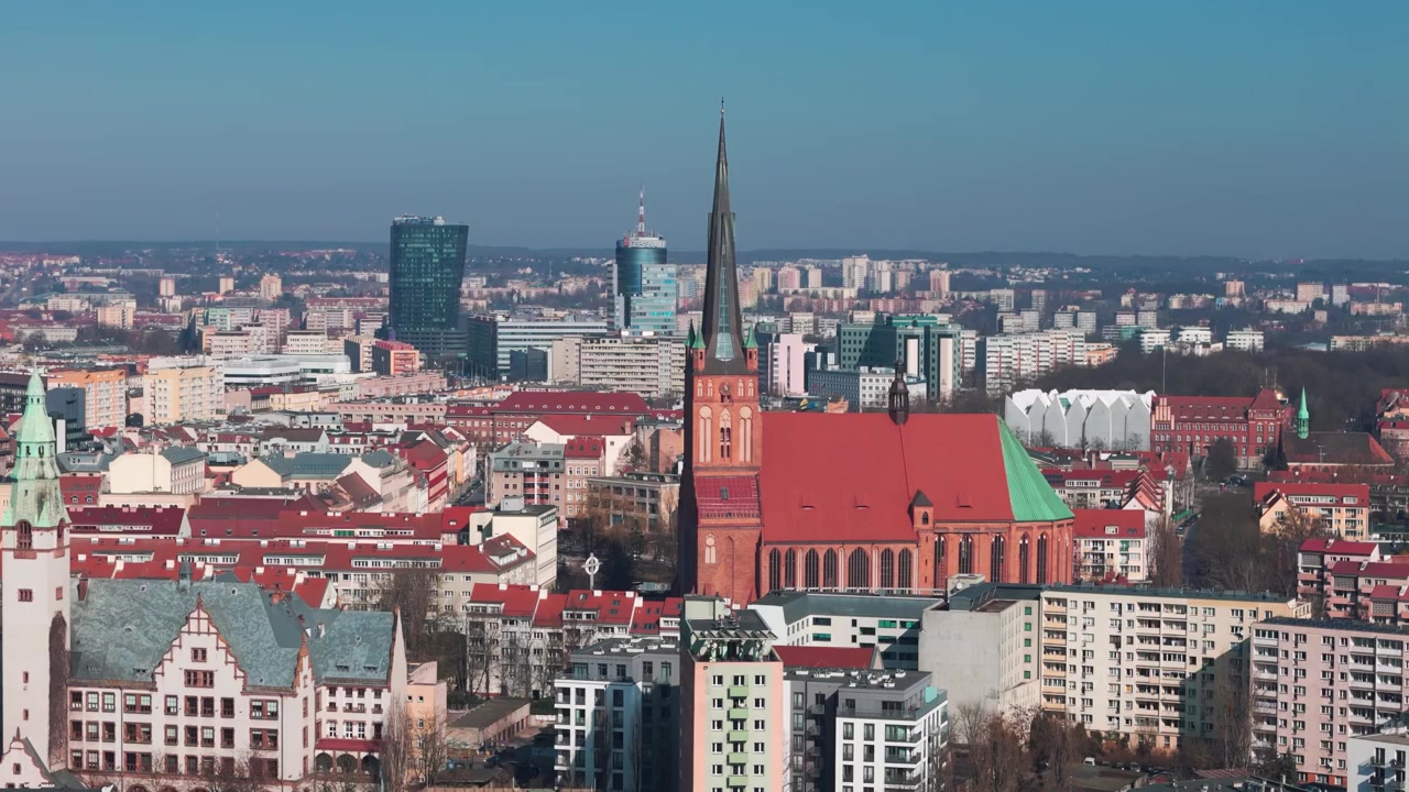 A wide aerial view of the Szczecin city skyline in Poland featuring the Cathedral Basilica of St. James the Apostle, Hanza Tower, and Pazim building under a clear blue sky.