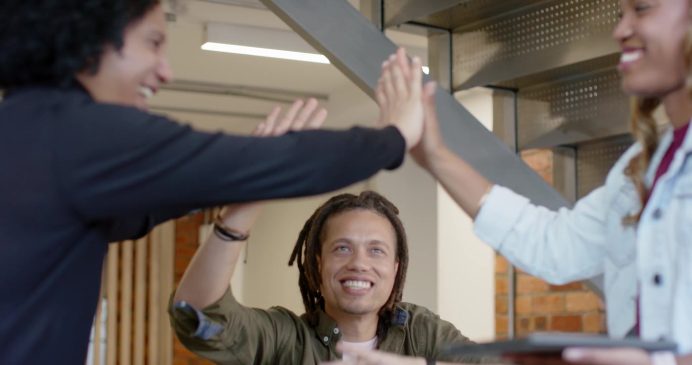 African American coworkers high-fiving and clapping at office after big win, woman holding tablet