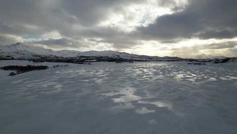 Aerial-view-pan-of-frozen-lake-reflection-with-sky,-Lofoten,-Norway