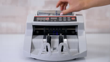 equipment for counting money. wad of hundred dollars are counted in a calculating machine. automatic equipment for banking financial transactions. female's hand puts money into electronic machine.