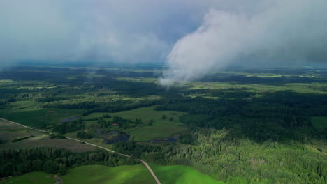 Una-Toma-En-ángulo-Alto-De-Un-Paisaje-Verde-Con-Un-Bosque,-Estanques-Y-Nubes-Brumosas