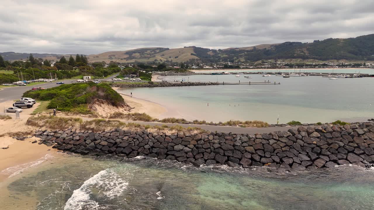 Drone footage captures Lorne's coastline with waves, sandy beaches, and a rocky breakwater under cloudy skies