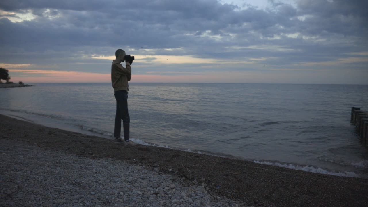 Man Leisurely Takes Photos Of The Beach On A Cloudy Sunset - wide shot