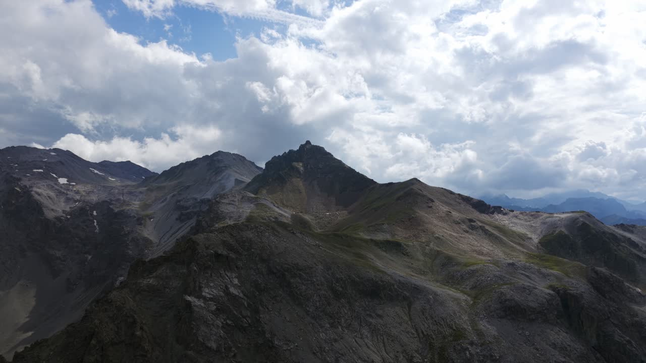 Aerial view of rugged mountain range at Umbrail Pass. Shows barren rocky peaks with patches of snow under cloudy sky. For nature or travel content, Swiss Alps, Switzerland