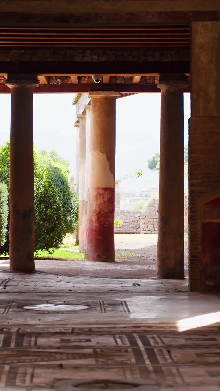 Vista vertical a través del suelo de un atrio conservado de Pompeya con baldosas de mosaico geométrico, orificios de cuencas circulares, columnas, luz solar cálida y detalles interiores de la antigua Roma