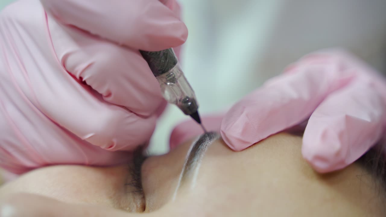 master is making permanent make-up of eyebrows with professional needle. Eyebrows shape correction. Cosmetology