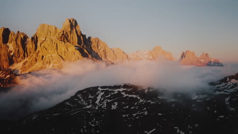 mystic aerial view showing dense fog and clouds hovering between golden lighting rocky mountains during sunset in italy