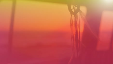 animation of dream catcher moving in wind with yellow to red hue with sunset in background