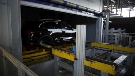 manufatured black car being moved, industry setting with conveyor system, dim lighting