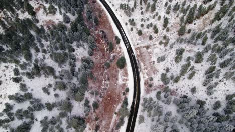 Vista-Aérea-De-Drones-De-La-Conducción-De-Automóviles-En-Una-Carretera-Invernal-Cubierta-De-Nieve-Negra-Rodeada-De-Pinos-Arbolados-Valle-De-Colinas-Cerca-De-Kittredge-Evergreen-Colorado