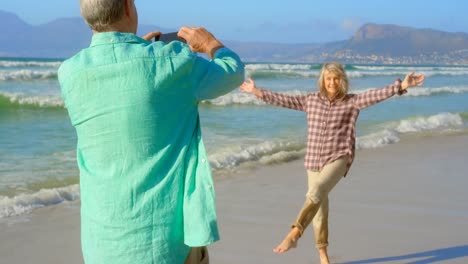 Rear-view-of-active-senior-Caucasian-man-clicking-photos-of-senior-woman-with-mobile-phone-on-the-be