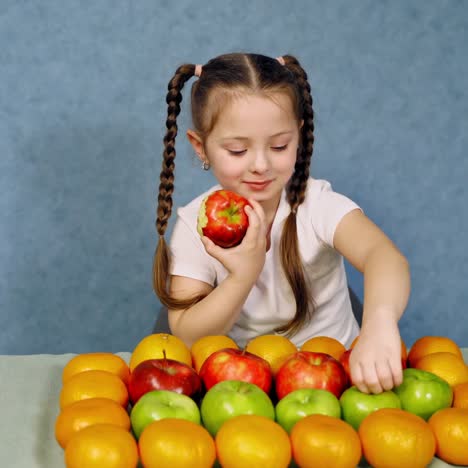 little girl eating juicy apple. fresh organic fruit nicely placed on the table. happy small girl with ripe fruits on blue background.