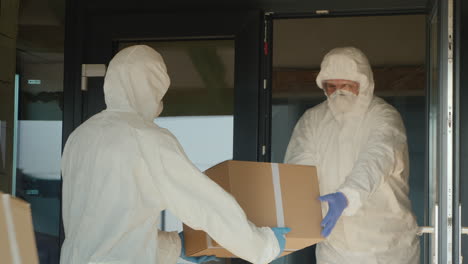 men in biological protection suits load boxes of medicine to hospital warehouse