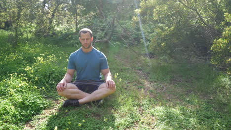 Un-Hombre-Sentado-En-Una-Pose-De-Meditación-En-Un-Prado-Verde-Y-Soleado-Practicando-Ejercicios-De-Respiración-Profunda-Para-Reducir-El-Estrés-Y-Aumentar-La-Salud-Mental-A-Cámara-Lenta