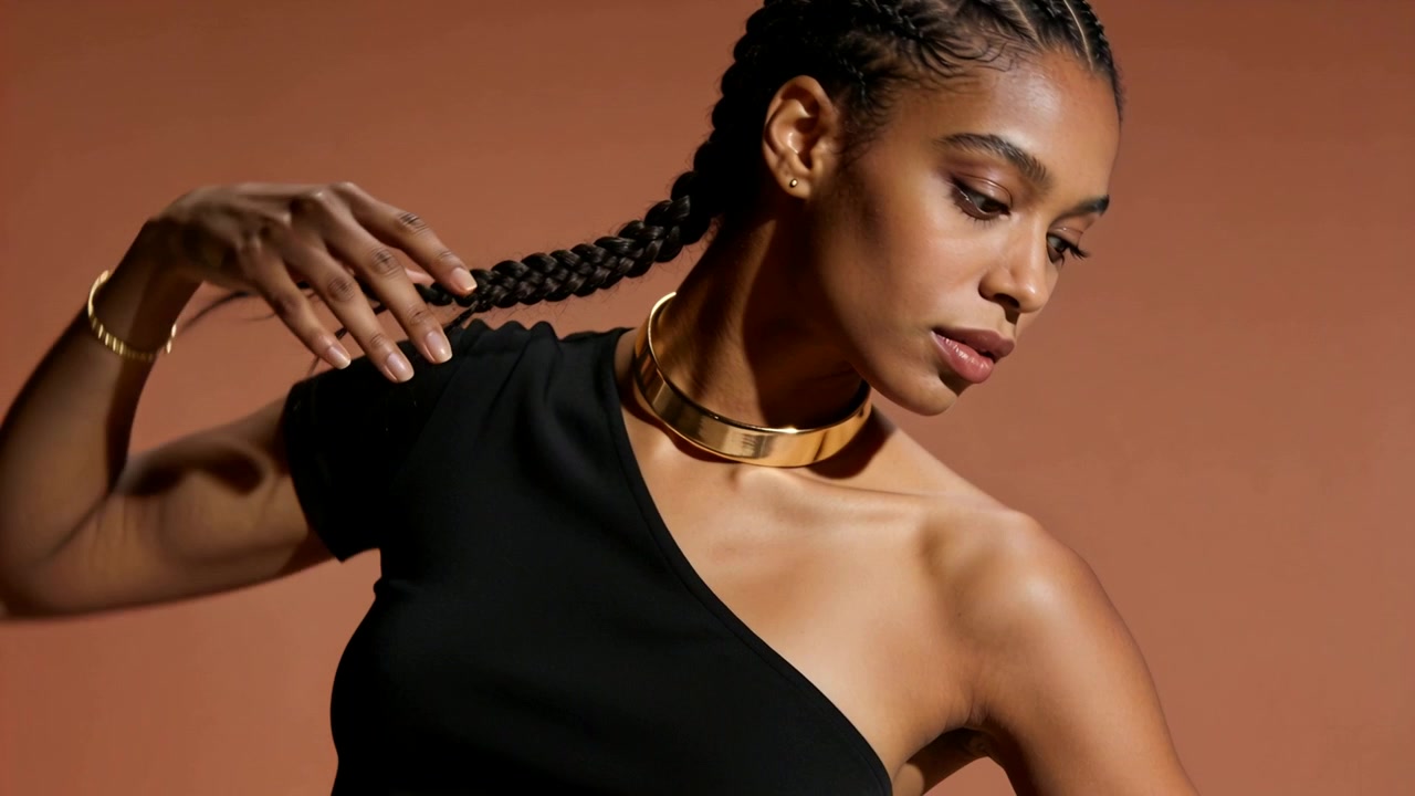 Starting hand near braid, model drawing braid down in studio, showing one-shoulder top, gold choker