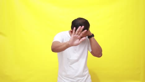 unhappy sad angry asian man close eyes and cover ears by hands being annoyed with loud noise, isolated yellow studio background